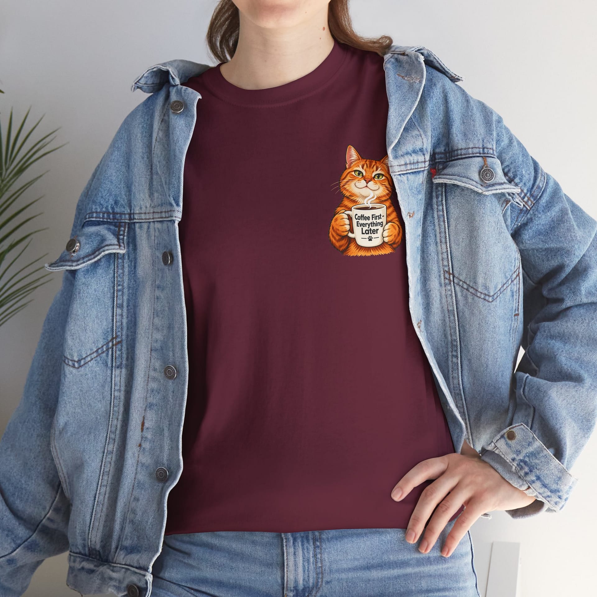 Cute orange cat holding a ‘But First Coffee’ mug printed on a unisex T‑shirt