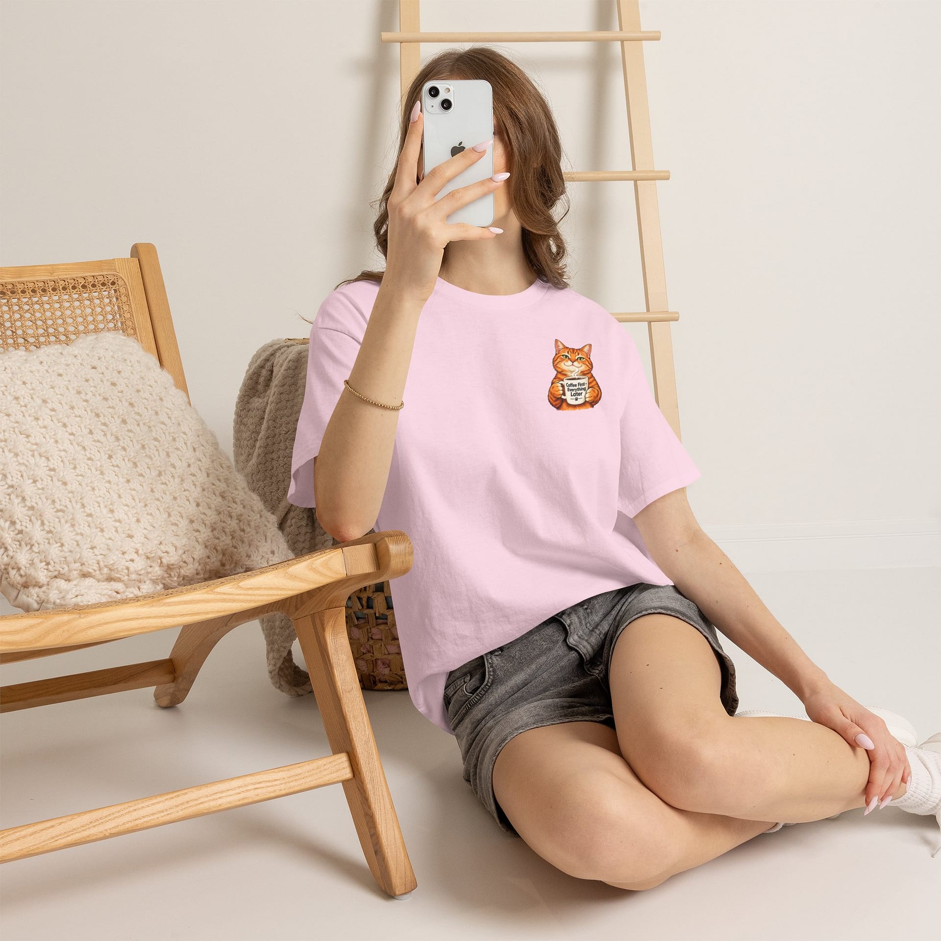 Cute orange cat holding a ‘But First Coffee’ mug printed on a unisex T‑shirt