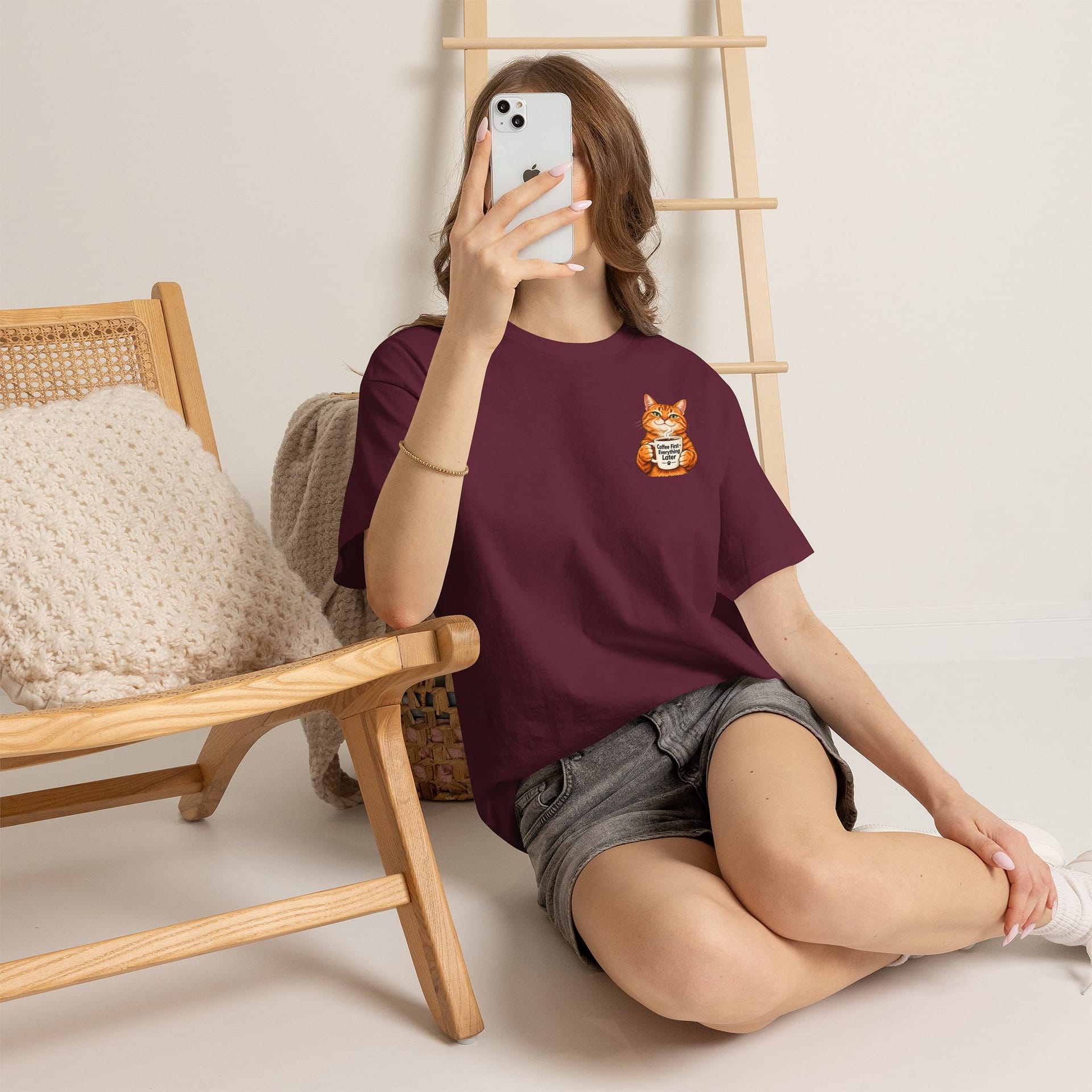 Cute orange cat holding a ‘But First Coffee’ mug printed on a unisex T‑shirt