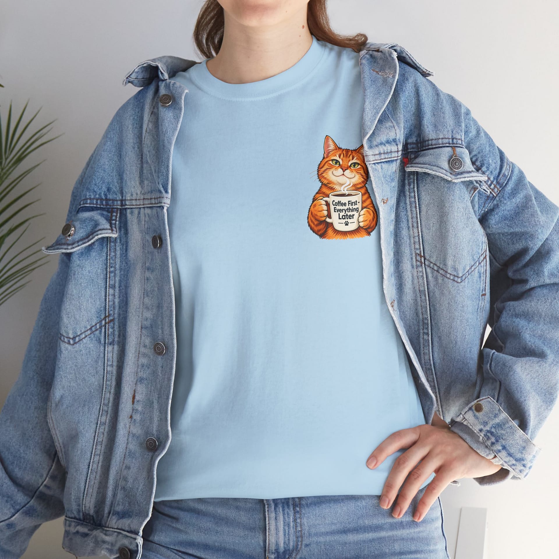 Cute orange cat holding a ‘But First Coffee’ mug printed on a unisex T‑shirt