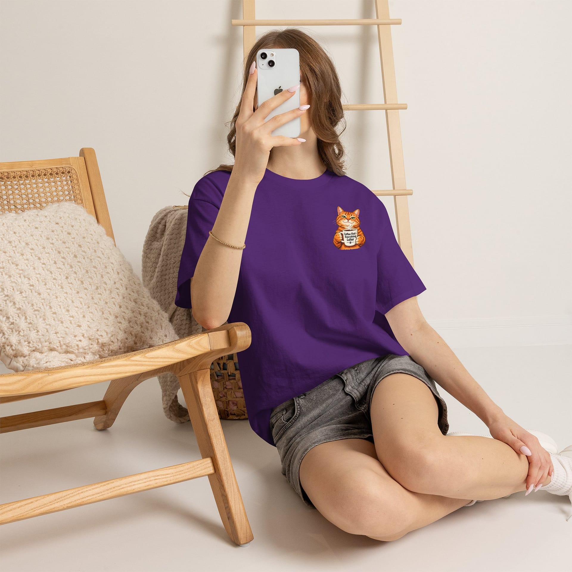 Cute orange cat holding a ‘But First Coffee’ mug printed on a unisex T‑shirt