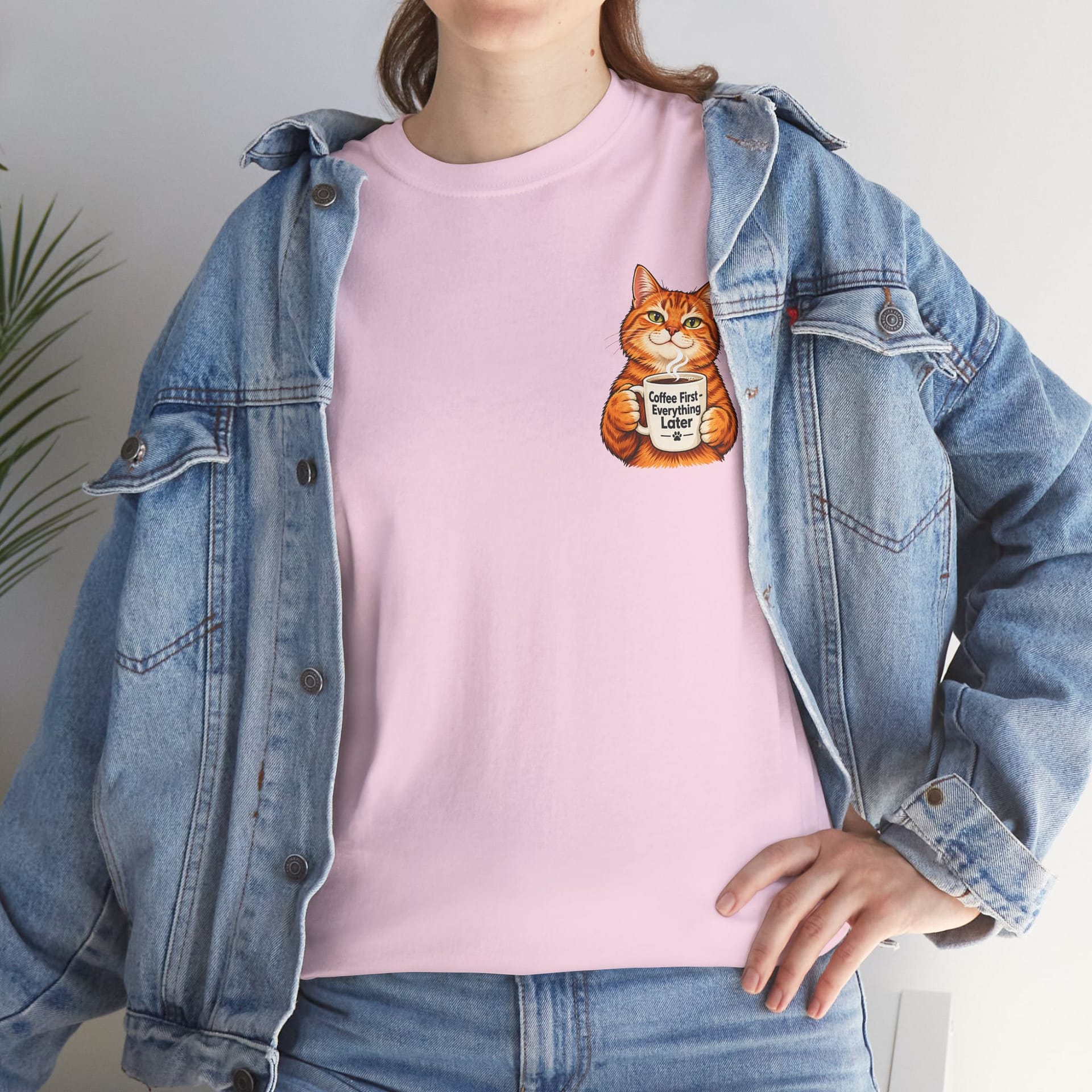 FCute orange cat holding a ‘But First Coffee’ mug printed on a unisex T‑shirt