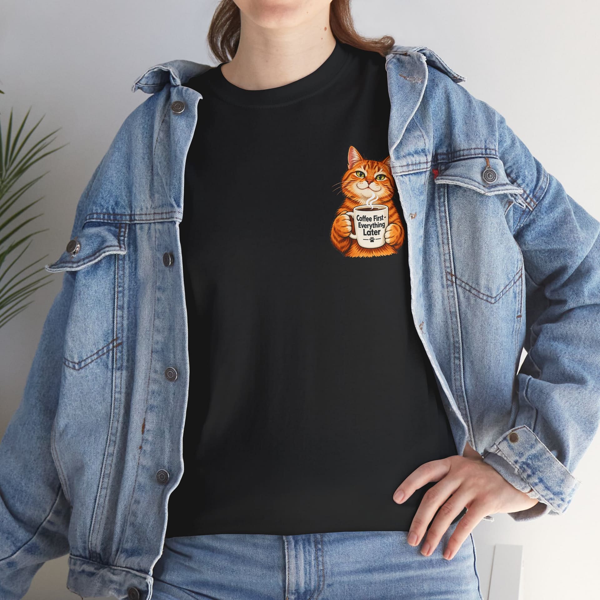 Cute orange cat holding a ‘But First Coffee’ mug printed on a unisex T‑shirt