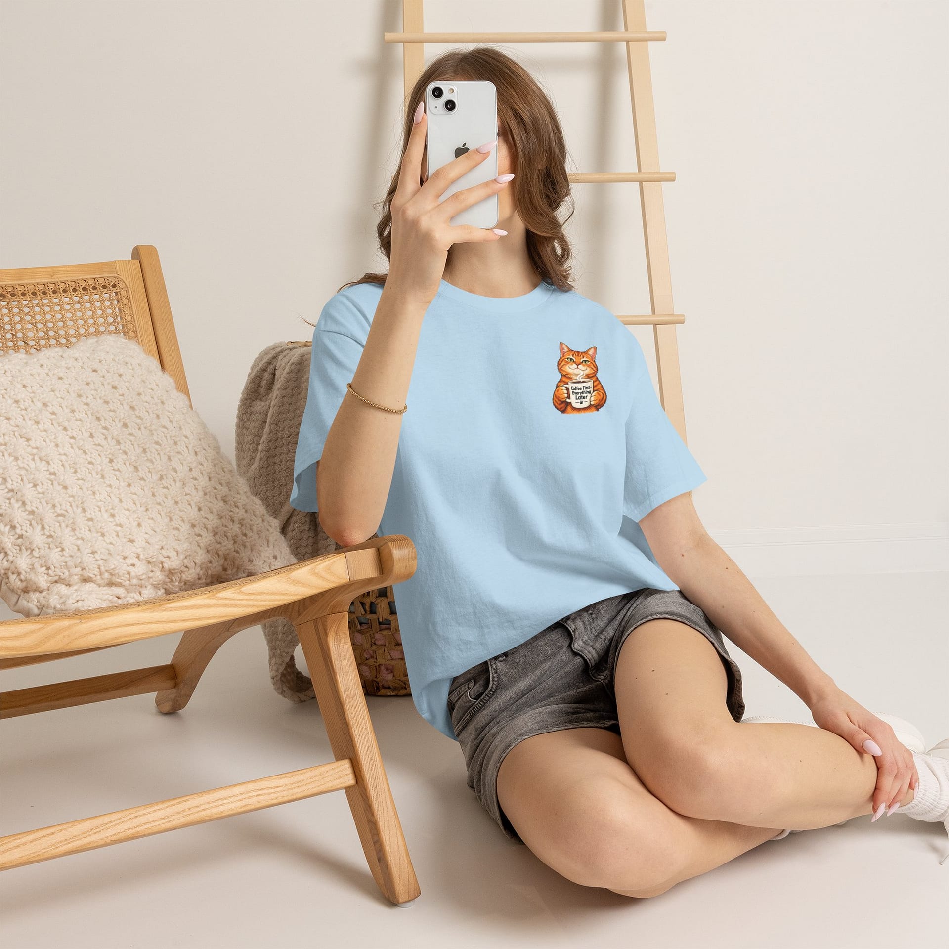 Cute orange cat holding a ‘But First Coffee’ mug printed on a unisex T‑shirt