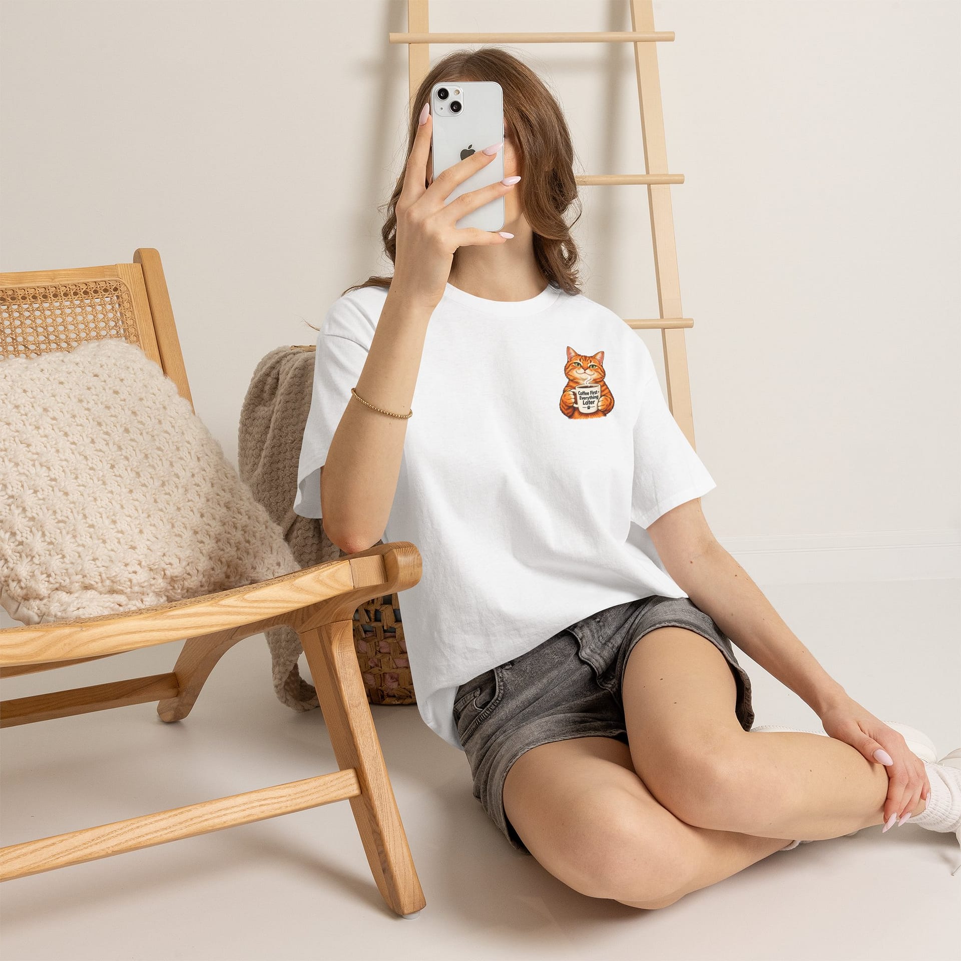 Cute orange cat holding a ‘But First Coffee’ mug printed on a unisex T‑shirt