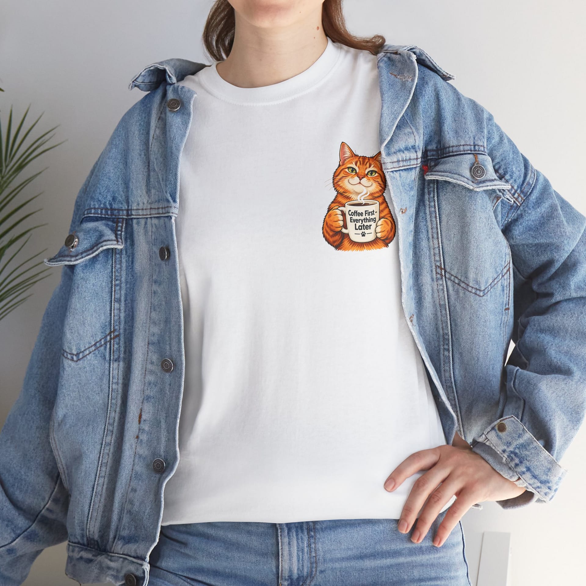 Cute orange cat holding a ‘But First Coffee’ mug printed on a unisex T‑shirt