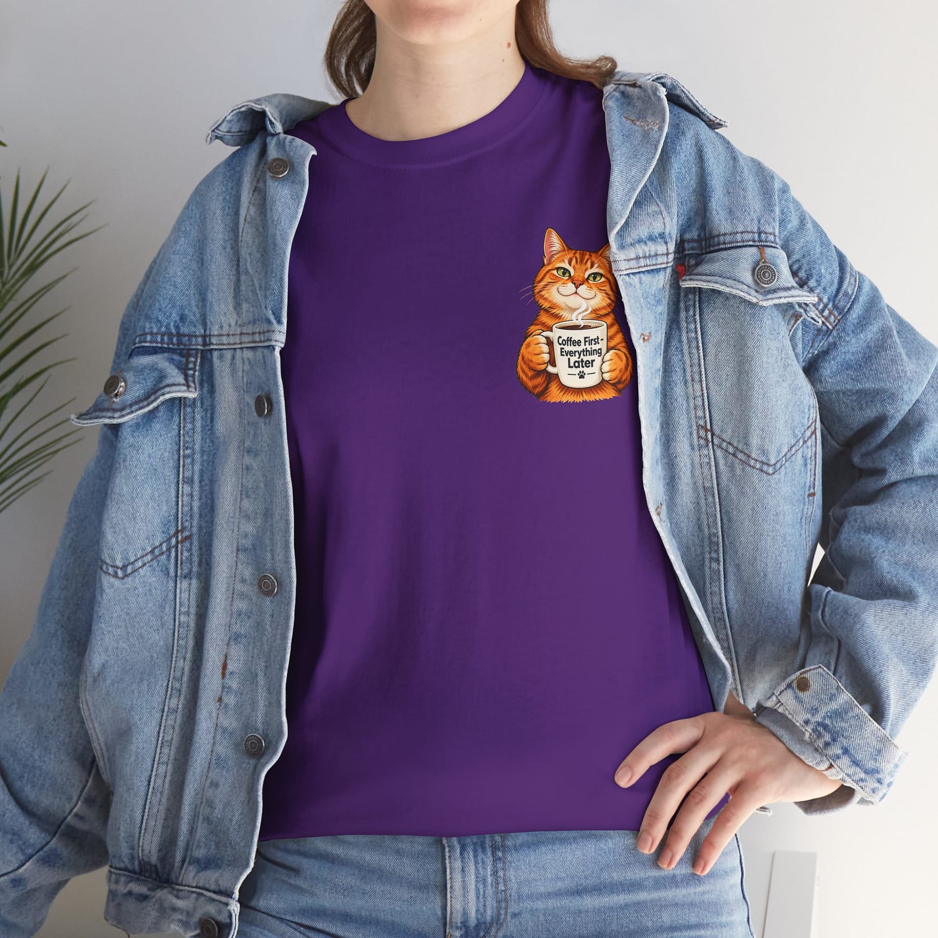 Cute orange cat holding a ‘But First Coffee’ mug printed on a unisex T‑shirt