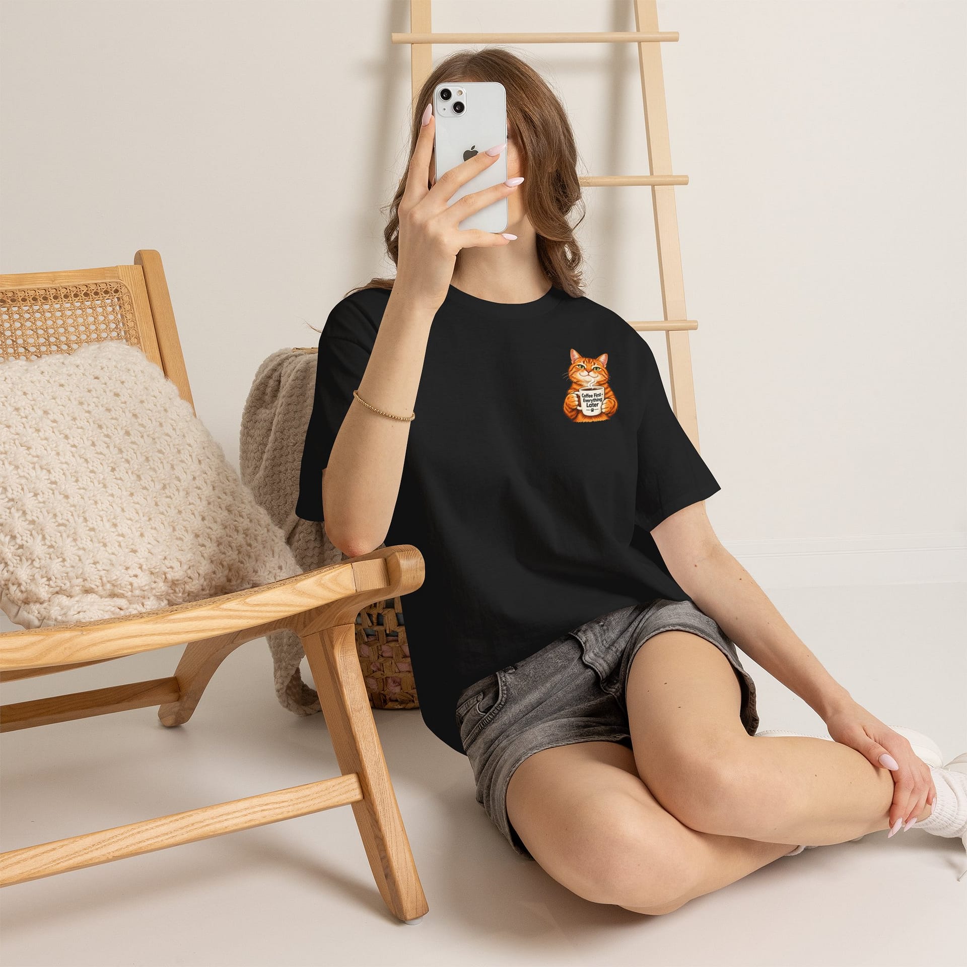 Cute orange cat holding a ‘But First Coffee’ mug printed on a unisex T‑shirt